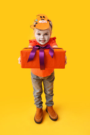 Little girl dressed for Halloween with gift on yellow backgroundの写真素材