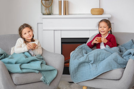 Cute little girls with cups of hot tea sitting at homeの写真素材