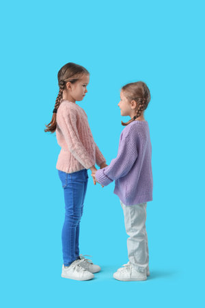 Cute little girls in warm sweaters holding hands on blue backgroundの写真素材