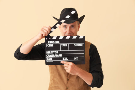 Mature actor dressed as cowboy with clapperboard on beige backgroundの写真素材
