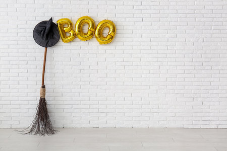 Broom, hat and text BOO made of balloons hanging on light brick wall in roomの写真素材