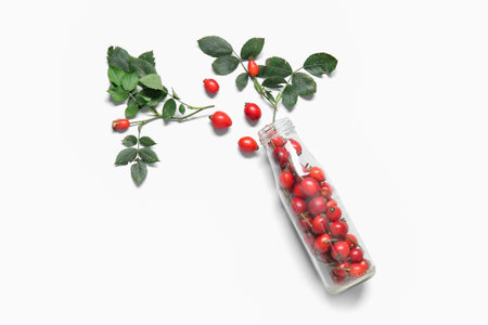 Bottle with fresh rose hip berries and leaves on white backgroundの写真素材