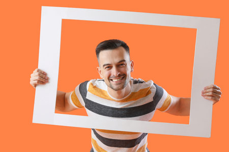 Happy young man with frame on orange background
