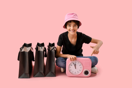Little boy with clock and shopping bags sitting on pink backgroundの写真素材