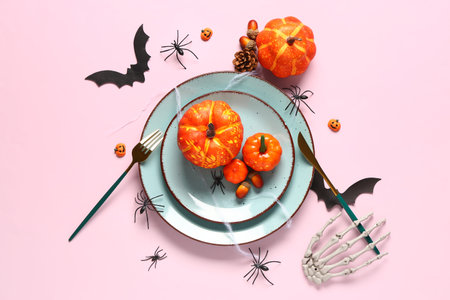 Halloween table setting with pumpkins and spiders on pink background