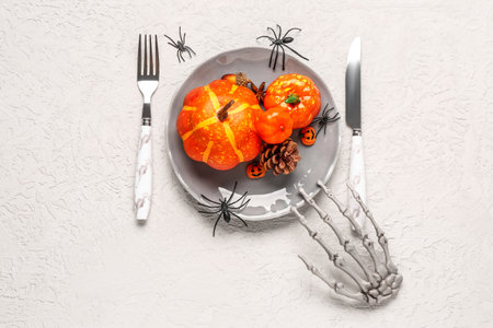 Halloween table setting with pumpkins, spiders and skeleton hand on white grunge backgroundの写真素材