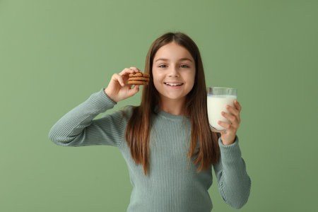 Little girl holding sweet chocolate cookies and glass of fresh milk on green backgroundの写真素材