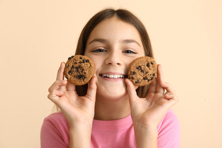 Little girl holding sweet chocolate cookies on beige background