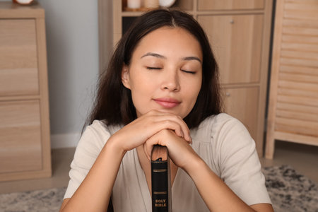 Beautiful young Asian woman with Bible in living room