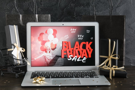 Laptop with Black Friday sale advertisement, gift boxes and confetti on dark wooden tableの写真素材