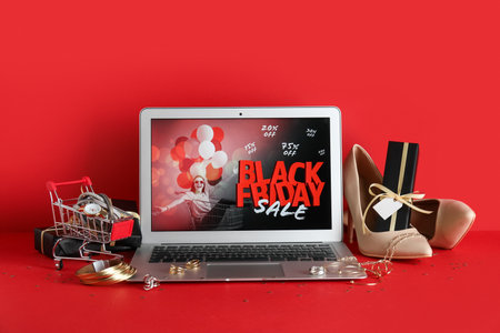 Laptop with Black Friday fashion sale advertisement, shoes, jewelry and gift box on red backgroundの写真素材