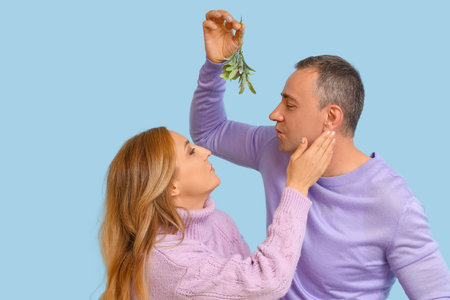 Mature couple kissing under mistletoe branch on blue backgroundの写真素材