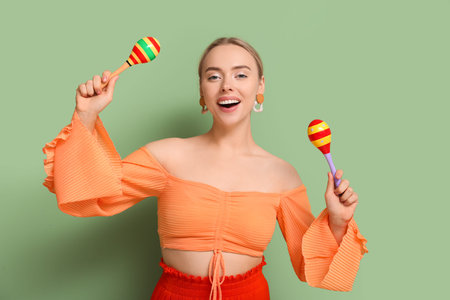 Pretty young woman with maracas on green background