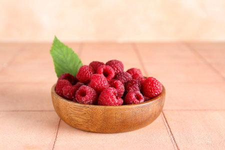 Wooden bowl with fresh ripe raspberries and leaf on pink tile table