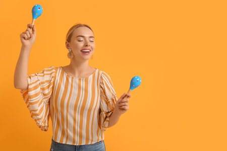 Pretty young woman with maracas on orange background