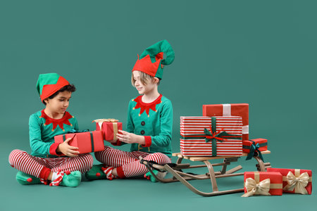 Cute little children in elves costumes with Christmas gifts and sledge on green backgroundの写真素材
