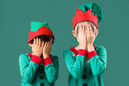 Cute little children in elves costumes closing eyes on green background