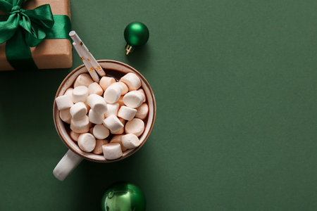 Cup of hot cocoa with marshmallows, Christmas balls and gift box on green backgroundの写真素材