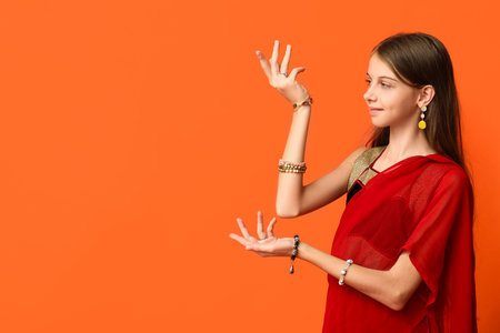Cute little Indian girl in sari dancing on orange background. Divaly celebrationの写真素材