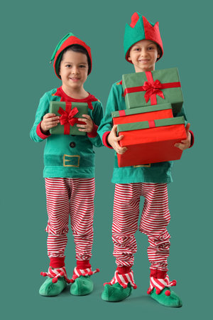 Cute little boys in elf costumes with Christmas presents on green background