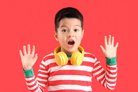 Shocked little Asian boy with headphones on red backgroundの写真素材