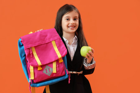 Cute little schoolgirl with backpack and apple on orange backgroundの写真素材