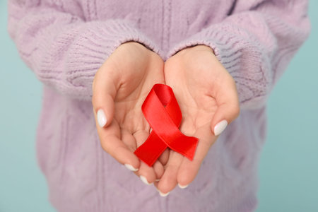 Woman holding red ribbon on blue background, closeup. World AIDS Day concept