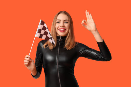 Beautiful young woman with racing flag showing ok gesture on red backgroundの写真素材