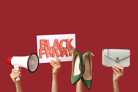 Female hands holding poster with text BLACK FRIDAY, megaphone and women accessories on red backgroundの写真素材