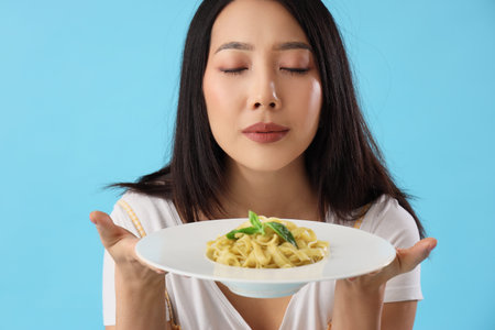 Young Asian woman with tasty pasta on blue background, closeupの写真素材