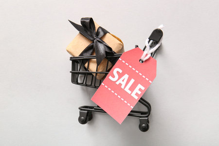 Small shopping cart, gift box and tag with text SALE on gray background. Cyber Monday sale