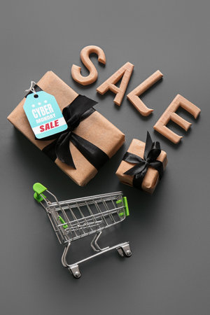 Composition with small shopping cart, gift boxes and word SALE on gray background. Cyber Mondayの写真素材