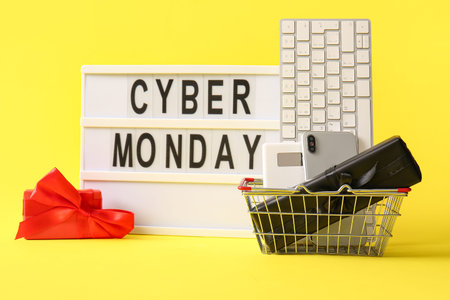 Board with text CYBER MONDAY, gadgets and gift boxes on yellow background