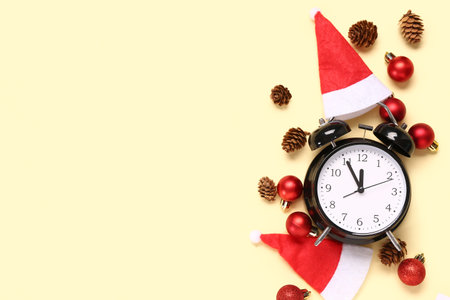 Christmas composition with alarm clock, Santa hats, baubles and pine cones on yellow background