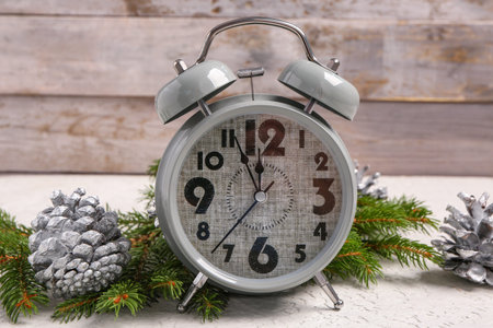 Christmas composition with alarm clock, fir tree branches and pine cones on white table