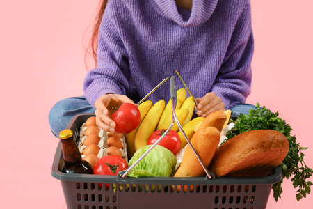 Woman putting fresh tomatoes in shopping basket on pink background