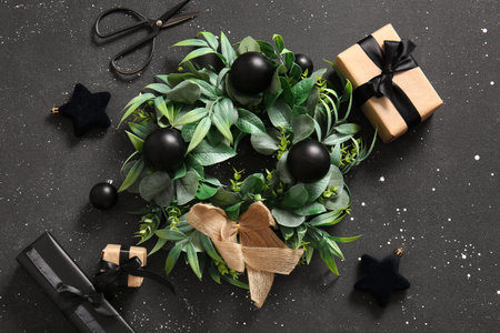 Christmas mistletoe wreath with balls and gift boxes on black background