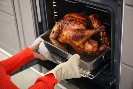 Woman taking tasty baked turkey from oven in kitchen. Thanksgiving Day celebrationの写真素材