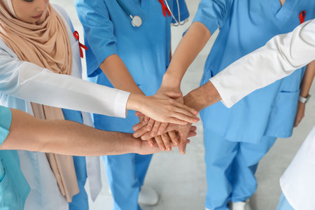 Team of doctors with red ribbons putting hands together in clinic, closeup. World AIDS Day conceptの写真素材