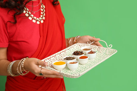 Beautiful Indian woman in sari holding tray with different spices on green backgroundの写真素材