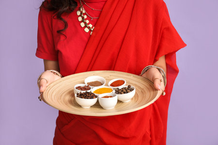 Beautiful Indian woman in sari holding plate with different spices on purple backgroundの写真素材