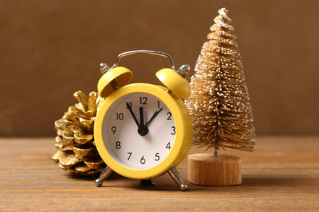 Christmas composition with yellow alarm clock, fir tree and pine cone on wooden table, closeup
