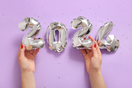 Female hands with figure 2024 made of foil balloons on lilac backgroundの写真素材