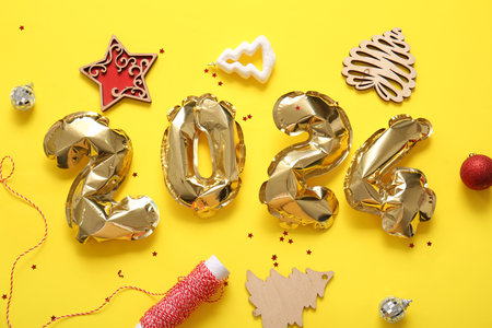 Figure 2024 made of foil balloons with Christmas decorations and confetti on yellow backgroundの写真素材
