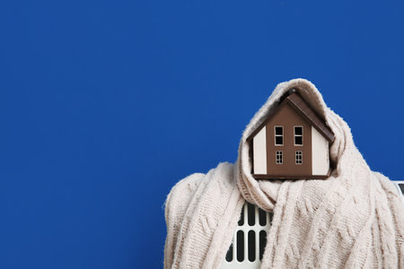 Figure of house with warm blanket on electric convector heater near blue wall at home. Heating saving conceptの写真素材
