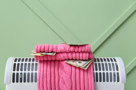 Warm scarf with money on electric convector heater near green wall at home. Heating saving concept