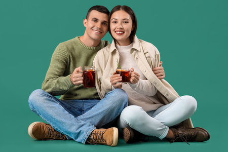 Happy couple with glasses of warm mulled wine sitting on turquoise backgroundの写真素材