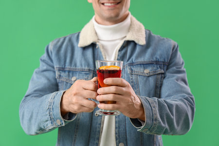 Handsome man with glass of mulled wine on green background, closeupの写真素材