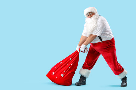 Santa Claus with bag full of Christmas gifts on blue backgroundの写真素材
