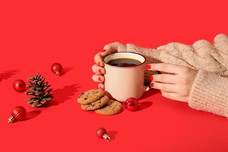 Female hands with red manicure, cup of coffee and Christmas decorations on color backgroundの写真素材